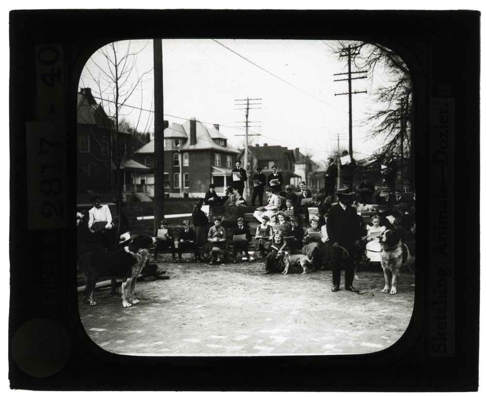 Fotografía horizontal en blanco y negro de estudiantes dibujando perros en un aula al aire libre de Unknown