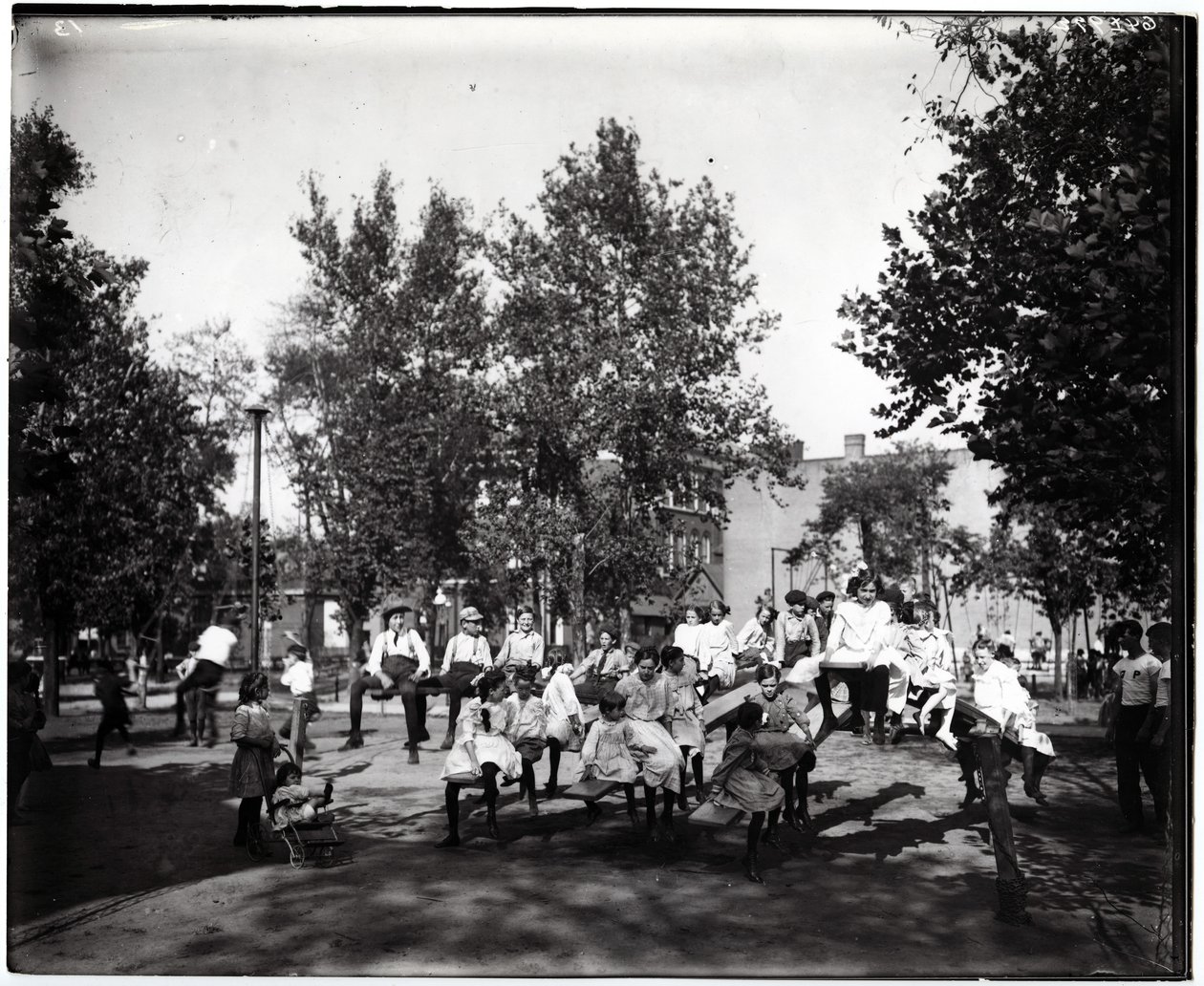 Fotografía horizontal en blanco y negro que muestra a niños jugando en sube y baja en un parque no identificado de Unknown