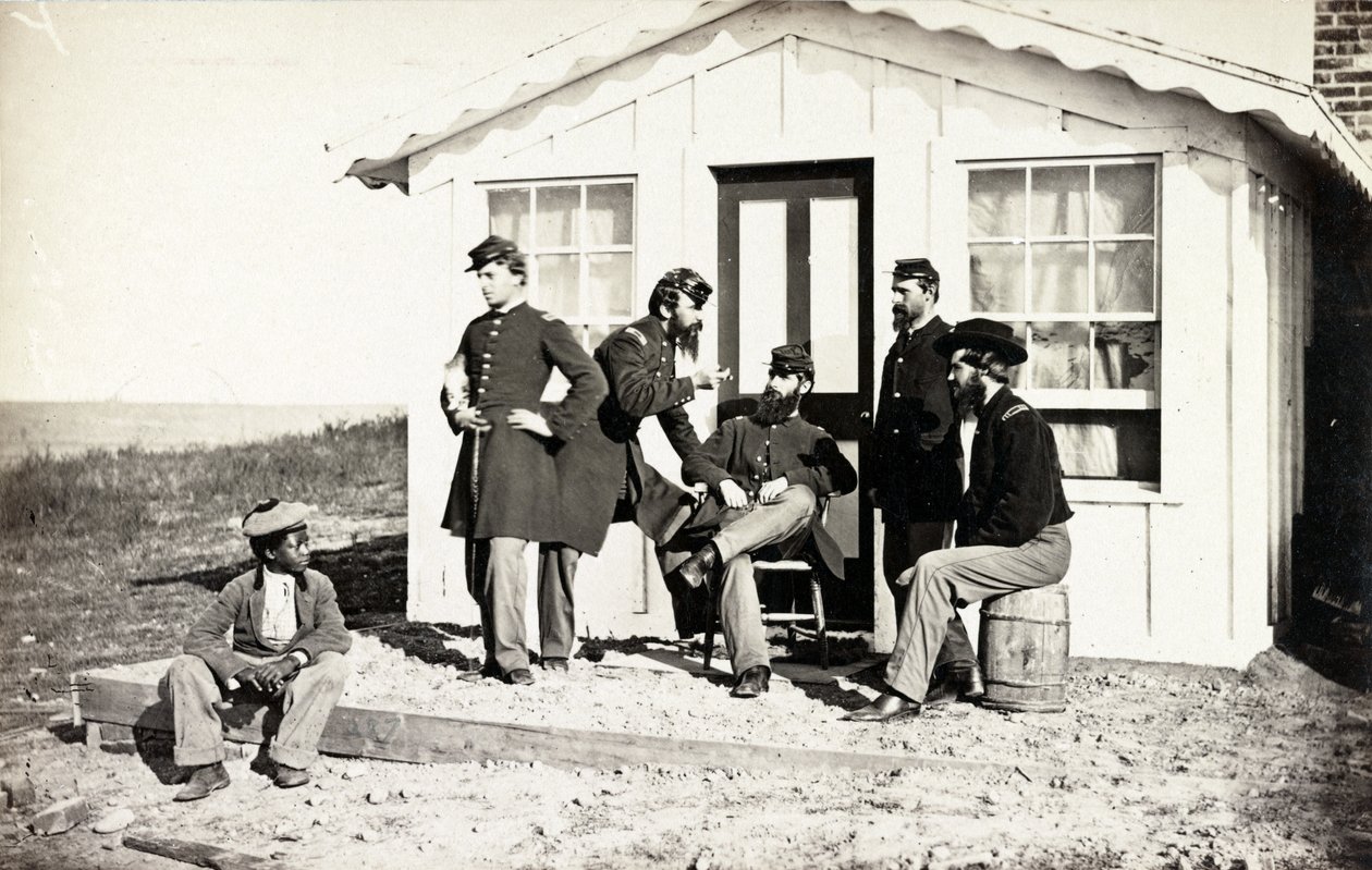 Cinco soldados de la Guerra Civil reunidos en el porche de tierra fuera de una casa, joven afroamericano sentado cerca de ellos, 1861-65 de American Photographer