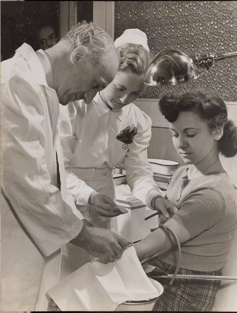 [Médico y enfermera insertan una aguja en el brazo de una mujer] de Arnold Eagle