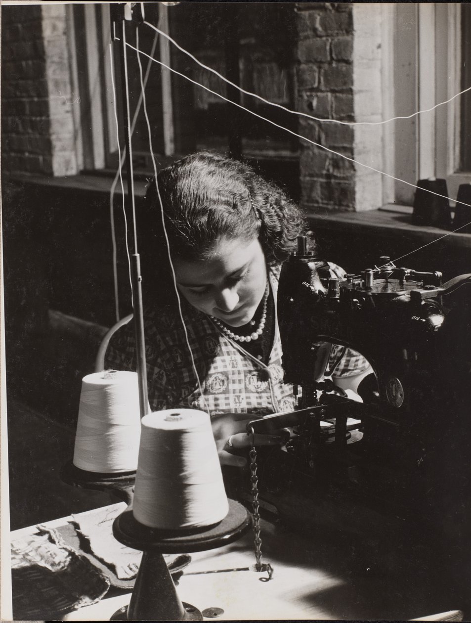 [La mujer utiliza una máquina de coser enhebrada con dos carretes de hilo blanco] de Arnold Eagle