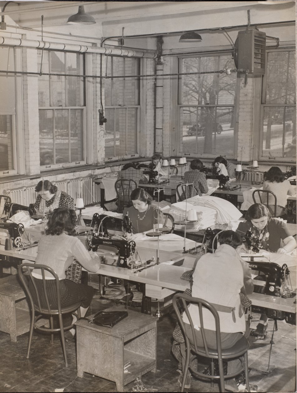 [Mujeres sentadas en escritorios trabajan en máquinas de coser] de Arnold Eagle