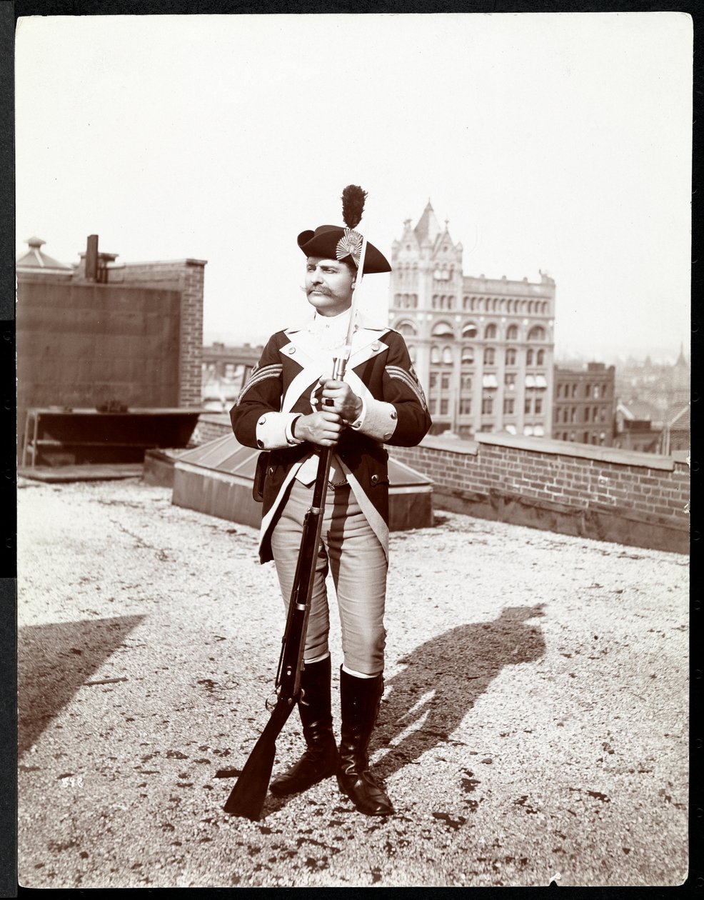Un hombre en un tejado vestido con un uniforme militar tradicional, sosteniendo un rifle, 1895 de Byron Company