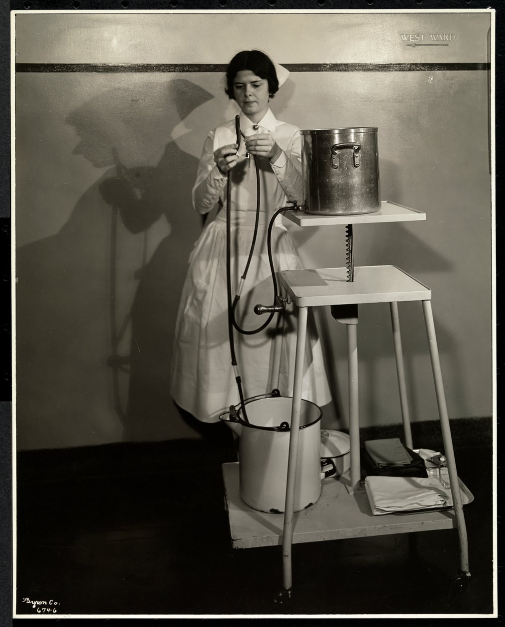 Una enfermera demostrando un aparato especial con tubos y cubos de suministro y desecho en el Sloan Maternity Hospital, Broadway y la calle 168, Nueva York, 1932 de Byron Company