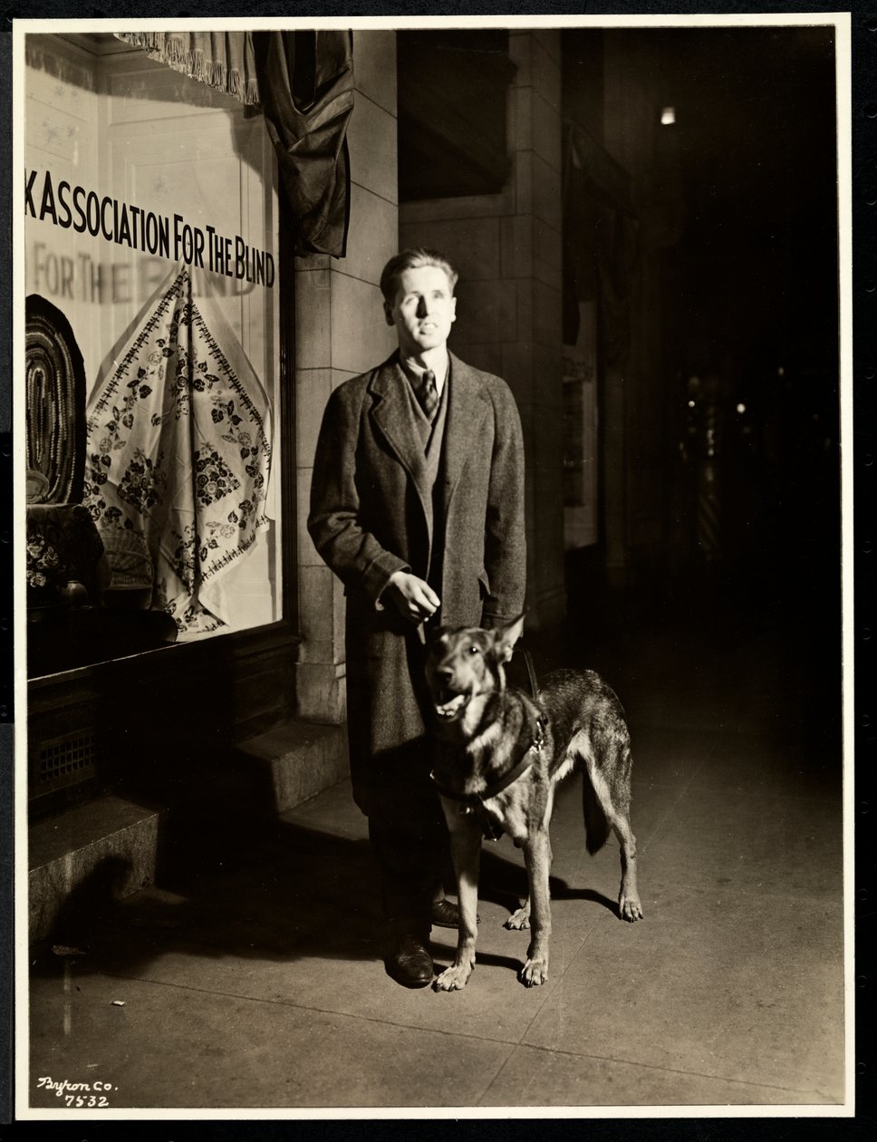 Hombre ciego y su perro guía en la acera frente a la Asociación para Ciegos de Nueva York, 111 East 59th Street, Nueva York, 1938 de Byron Company