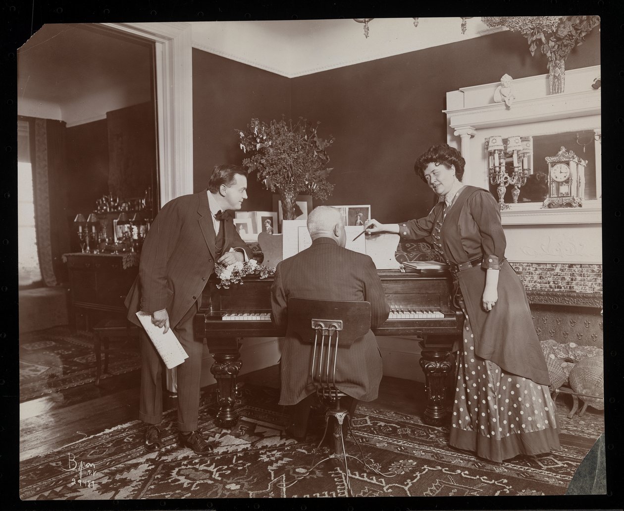 Clara De Regand señalando una partitura mientras un hombre toca el piano, 1910 de Byron Company