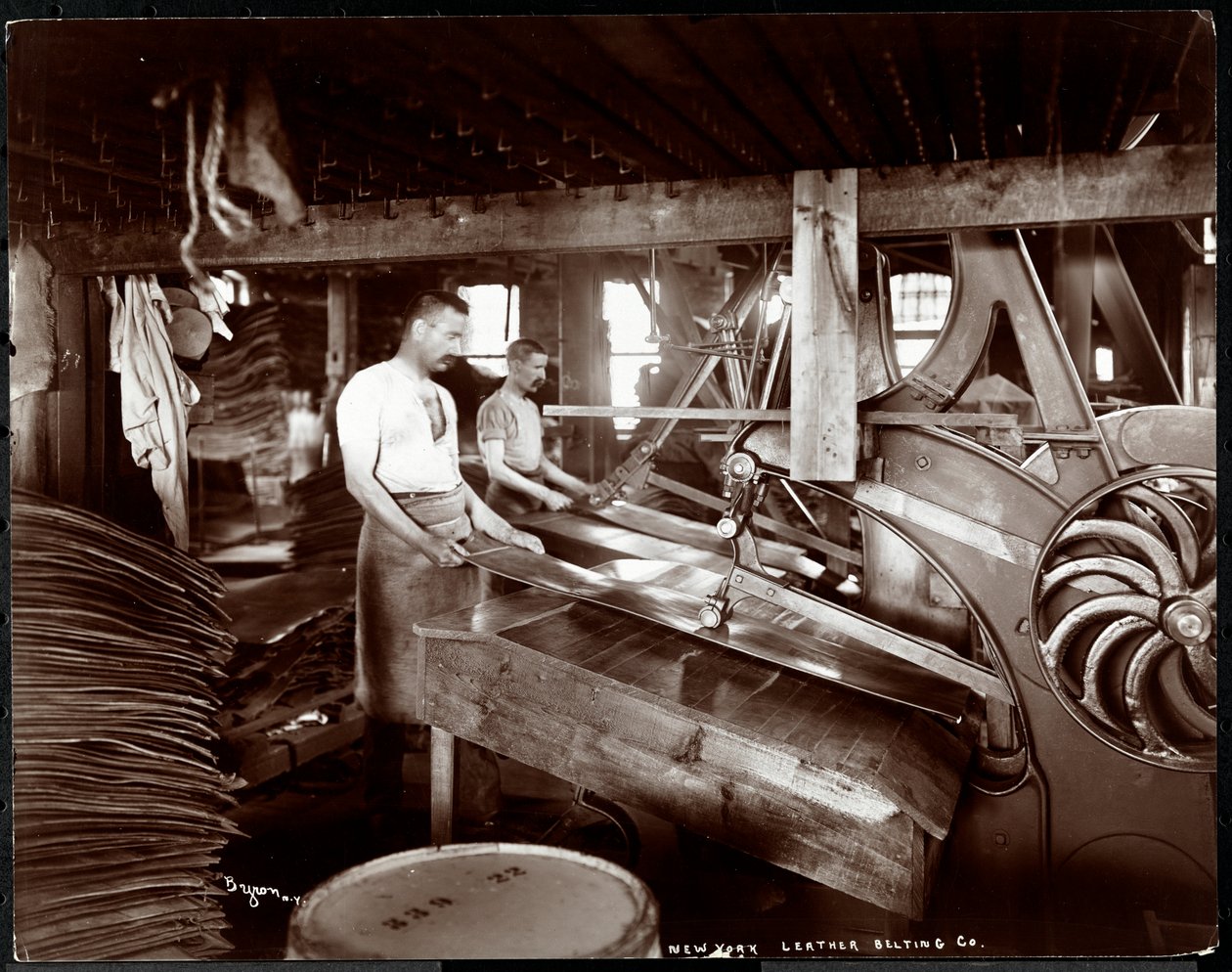 Vista interior de dos hombres trabajando con cuero y equipo pesado en la New York Leather Belting Co., Nueva York, 1905 de Byron Company