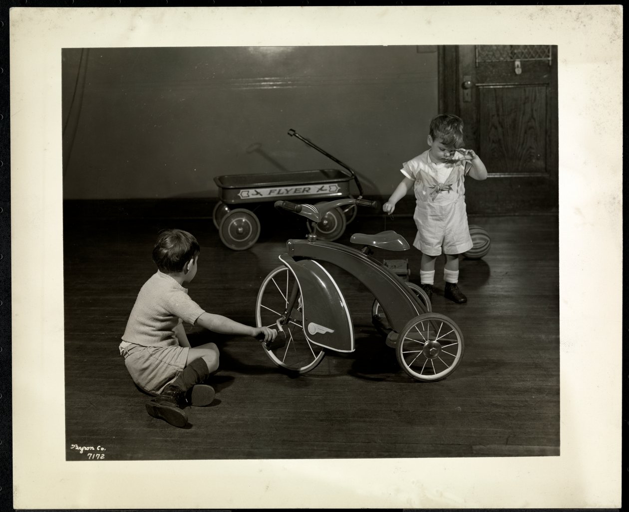 Dos niños ciegos jugando con un triciclo y un carro rojo en la Asociación para Ciegos de Nueva York, 111 East 59th Street, Nueva York, 1937 (impresión de gelatina de plata) de Byron Company
