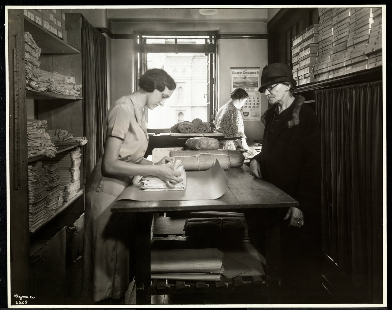 Joven envolviendo materiales de tela para que una trabajadora a domicilio los lleve, en la Asociación de Nueva York para Ciegos, 111 East 59th Street, Nueva York, 1931 de Byron Company