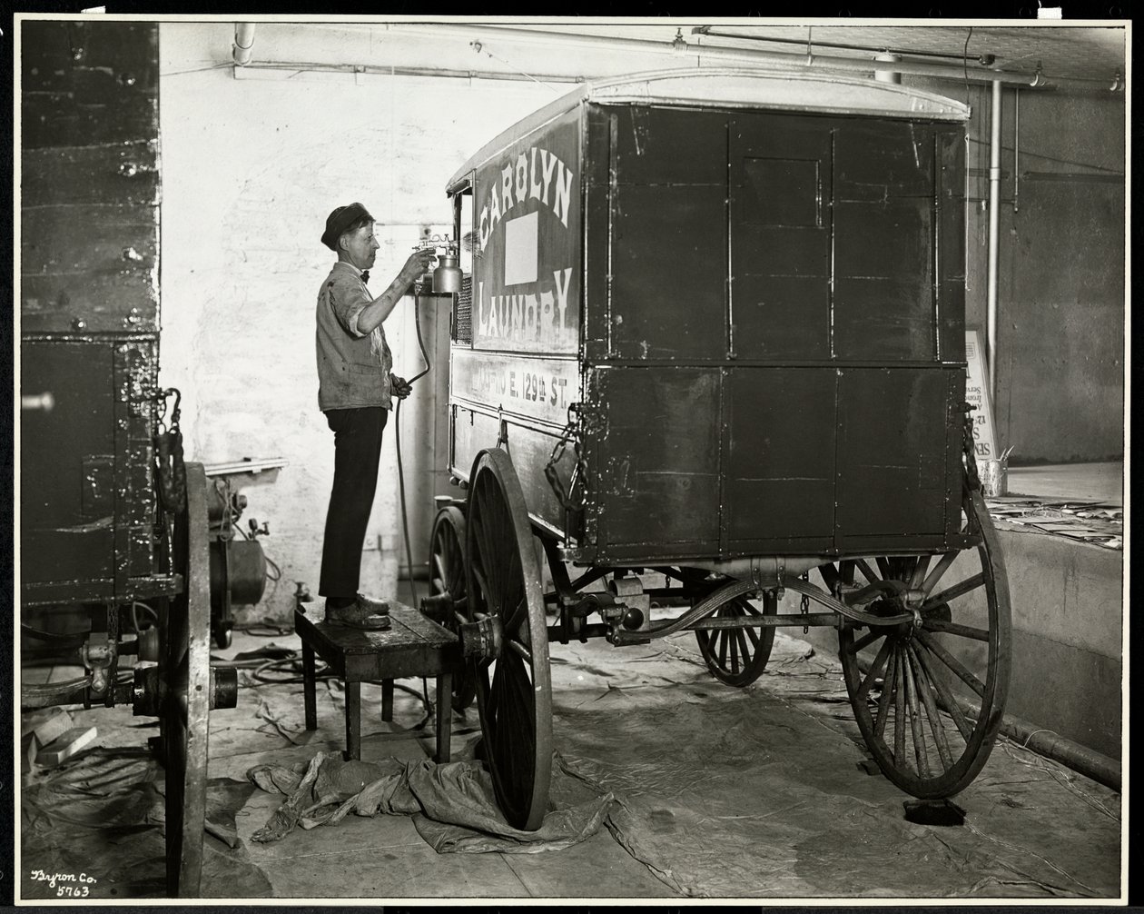Un hombre pintando con aerosol un carro de reparto de Carolyn Laundry en 111 East 128th Street, East Harlem, Nueva York, 1929 de Byron Company