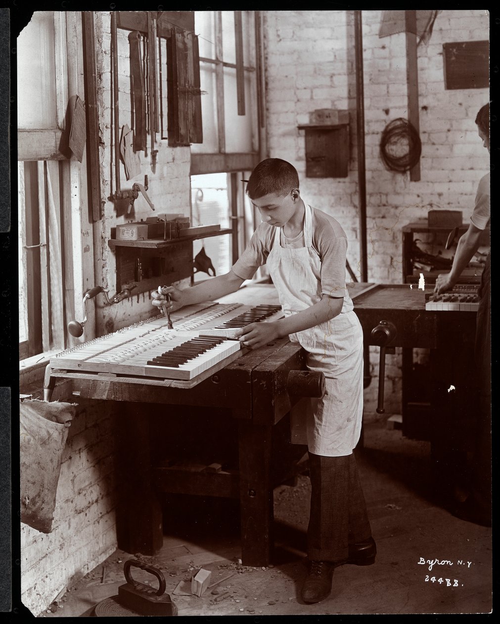 Un joven trabajando en la fábrica de Harrington Piano Co., 1907 de Byron Company
