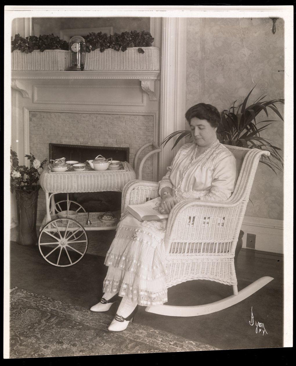 La Sra. Howard sentada con un libro en una mecedora en su casa en 200, 5th Avenue, Nueva York, 1915-6 de Byron Company
