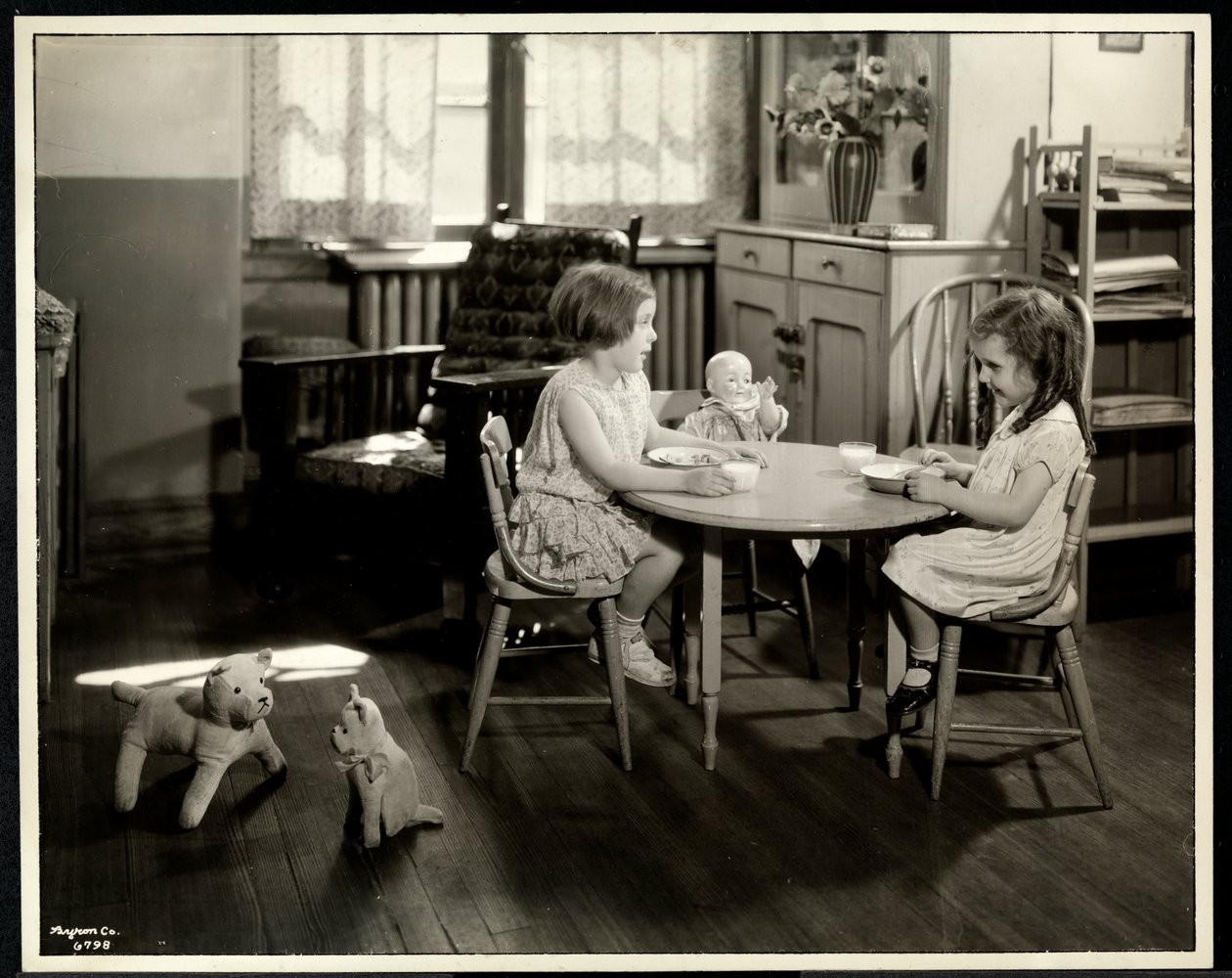 Dos niñas ciegas comiendo en una mesa pequeña con una muñeca en la Asociación para Ciegos de Nueva York, 111 East 59th Street, Nueva York, 1933 (impresión de gelatina de plata) de Byron Company