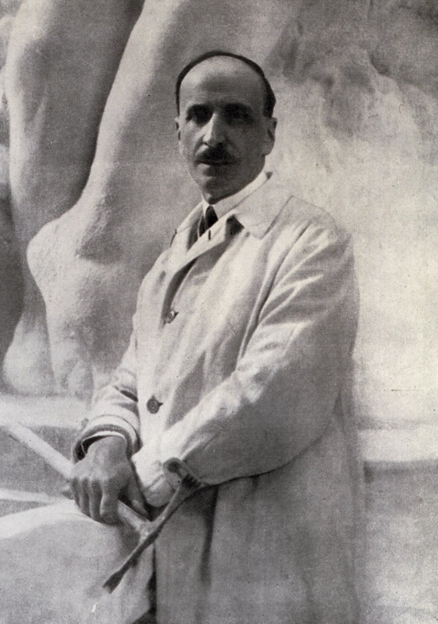 Retrato de tres cuartos del escultor Edoardo Rubino con martillo en mano. En el fondo se puede distinguir una escultura de Carlo Gherlone