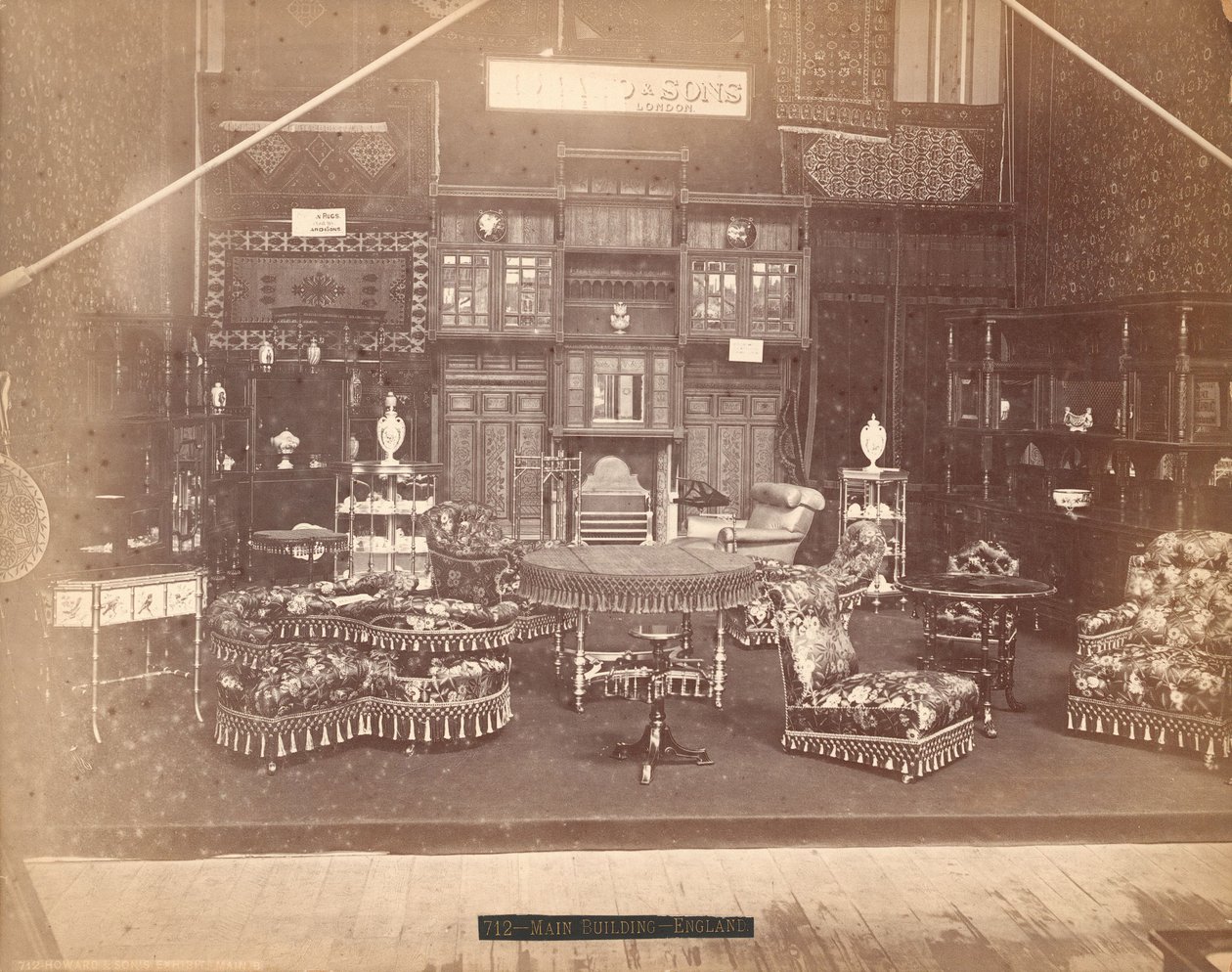 Exhibición de S. Howard & Sons -- Edificio Principal, Colección de muebles, incluyendo sillas tapizadas, mesas, una chimenea, gabinetes y estanterías. En las paredes hay alfombras, y en las mesas y estantes hay jarrones de Centennial Photographic Co.