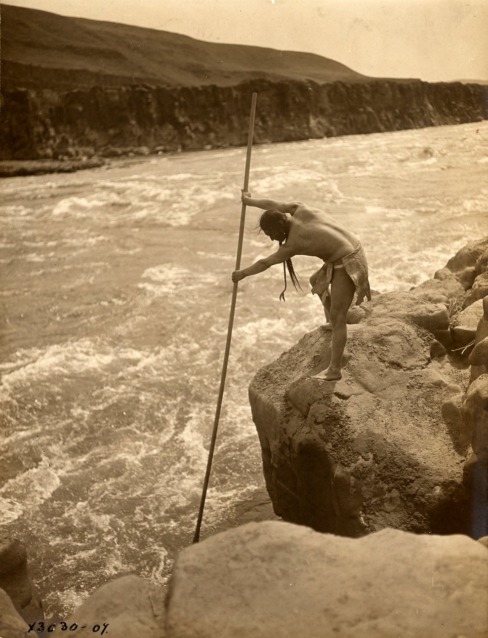 Indio tlakluit, de pie sobre una roca, pescando con una red, hacia 1910 (fotografía en blanco y negro). de Edward Sheriff Curtis