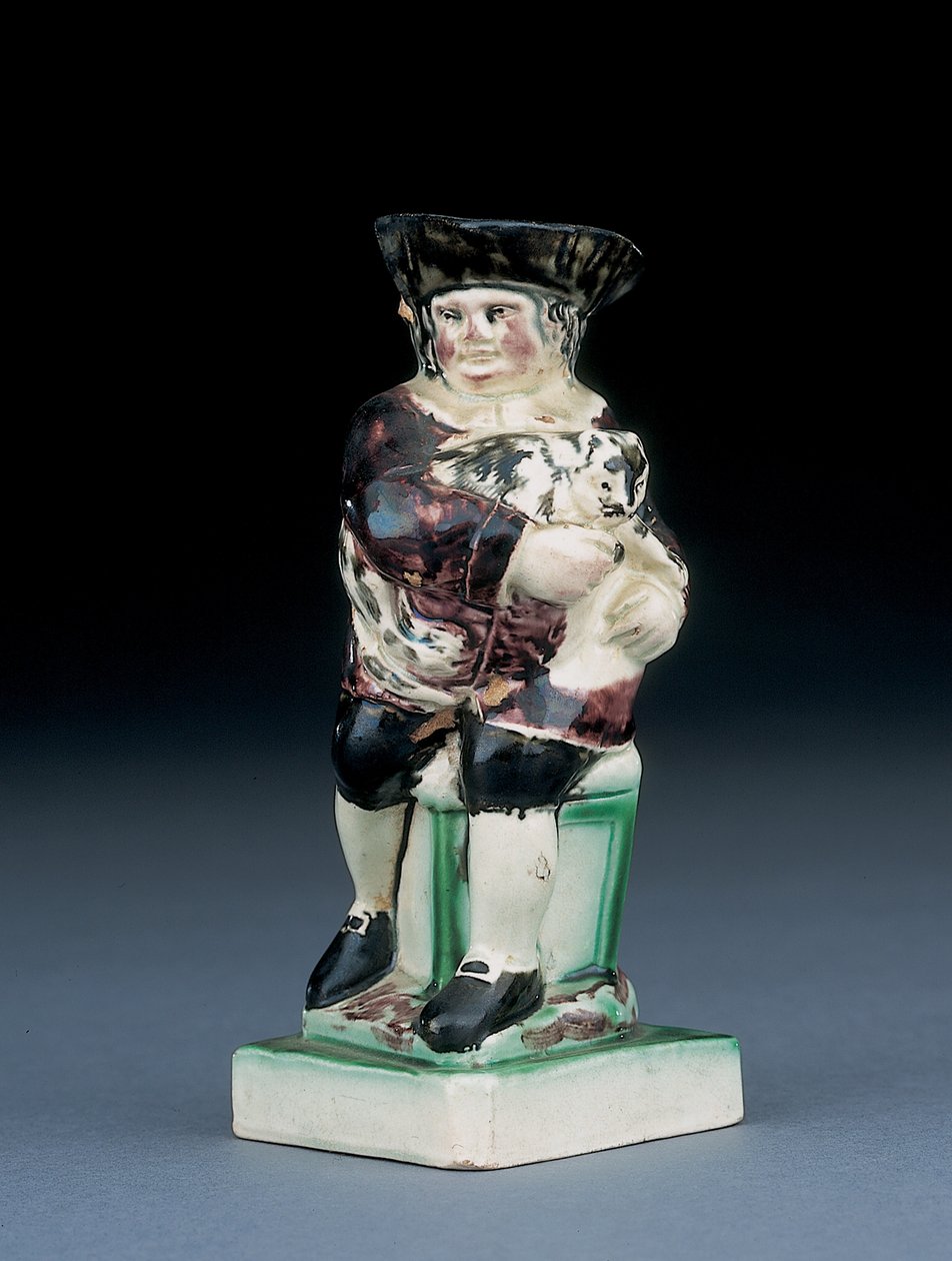 Jarra de Dick Whittington, moldeada levantándose de una silla de respaldo alto, sosteniendo a su gato, salpicada en ropa marrón, verde y negra, un escudo moldeado a su lado de English School