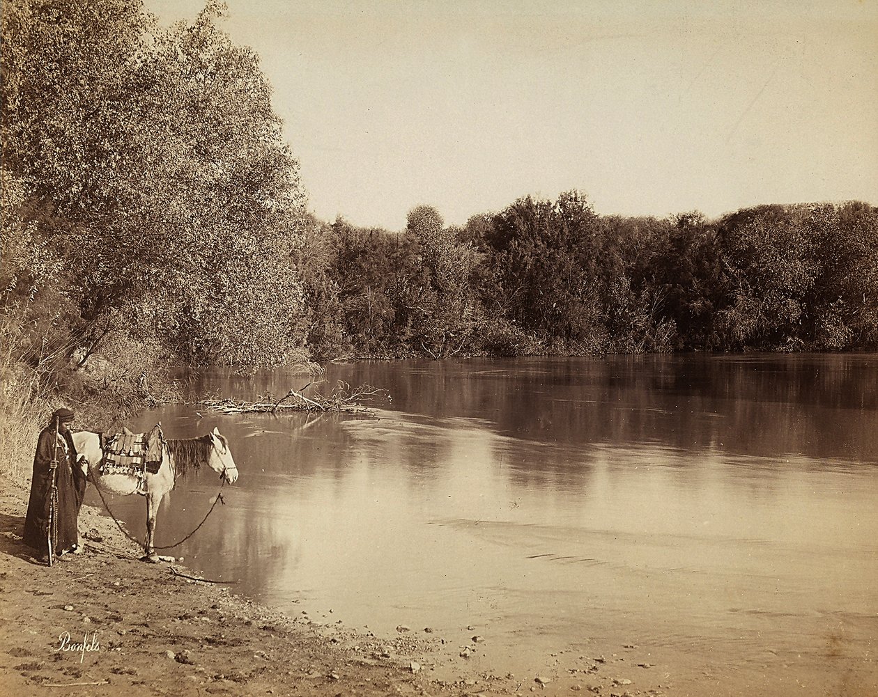 Un hombre con vestimenta tradicional con su caballo, frente a un lago en Egipto de Félix Bonfils