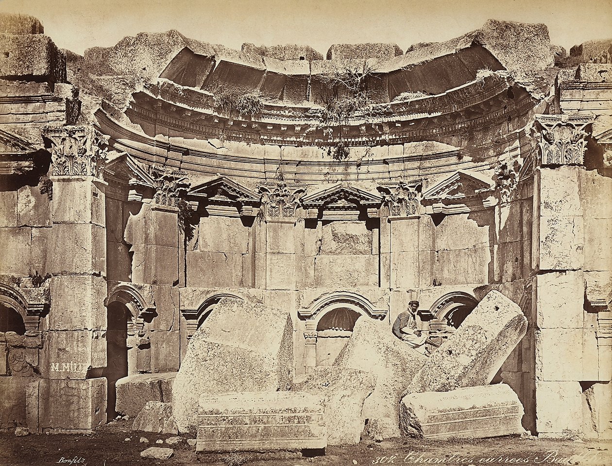 (detalle) de las llamadas "habitaciones" en la zona arqueológica de Heliópolis o Baalbek, antigua ciudad siria, ahora Líbano. Un hombre posa, sentado en las ruinas de Félix Bonfils