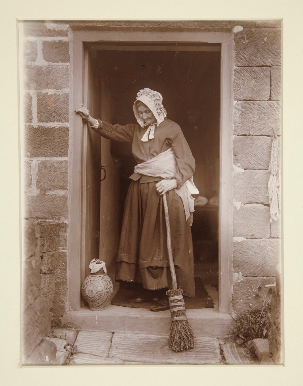 Una anciana con una botella de levadura en la puerta de una cabaña de Frank Meadow Sutcliffe