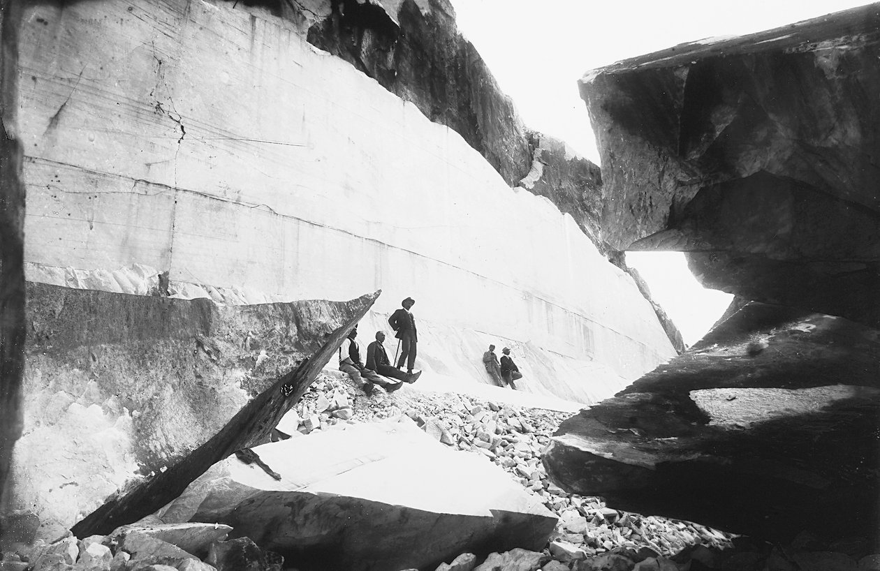 Algunos hombres sentados a lo largo de las paredes de una cantera de mármol, en los Alpes Apuanos (foto en b/n) de G. Armani