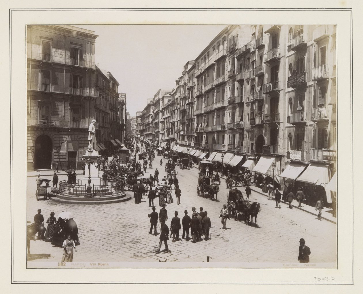 Vista de la Via Roma en Nápoles, con una estatua, tiendas, carruajes tirados por caballos y transeúntes de Giorgio Sommer