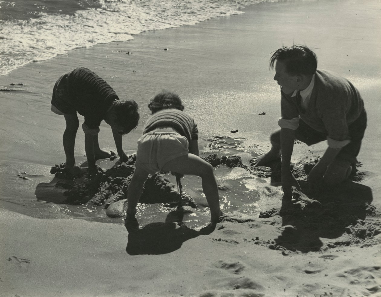 Tres niños jugando con arena en la playa. de Godfrey Macdominic