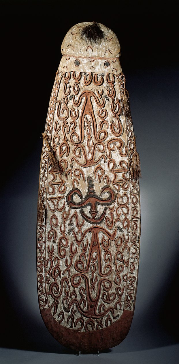 Escudo ovalado Asmat, tallado en relieve con ornamento de volutas que incorpora figuras altamente estilizadas, borlas trenzadas en el borde de Guinean New