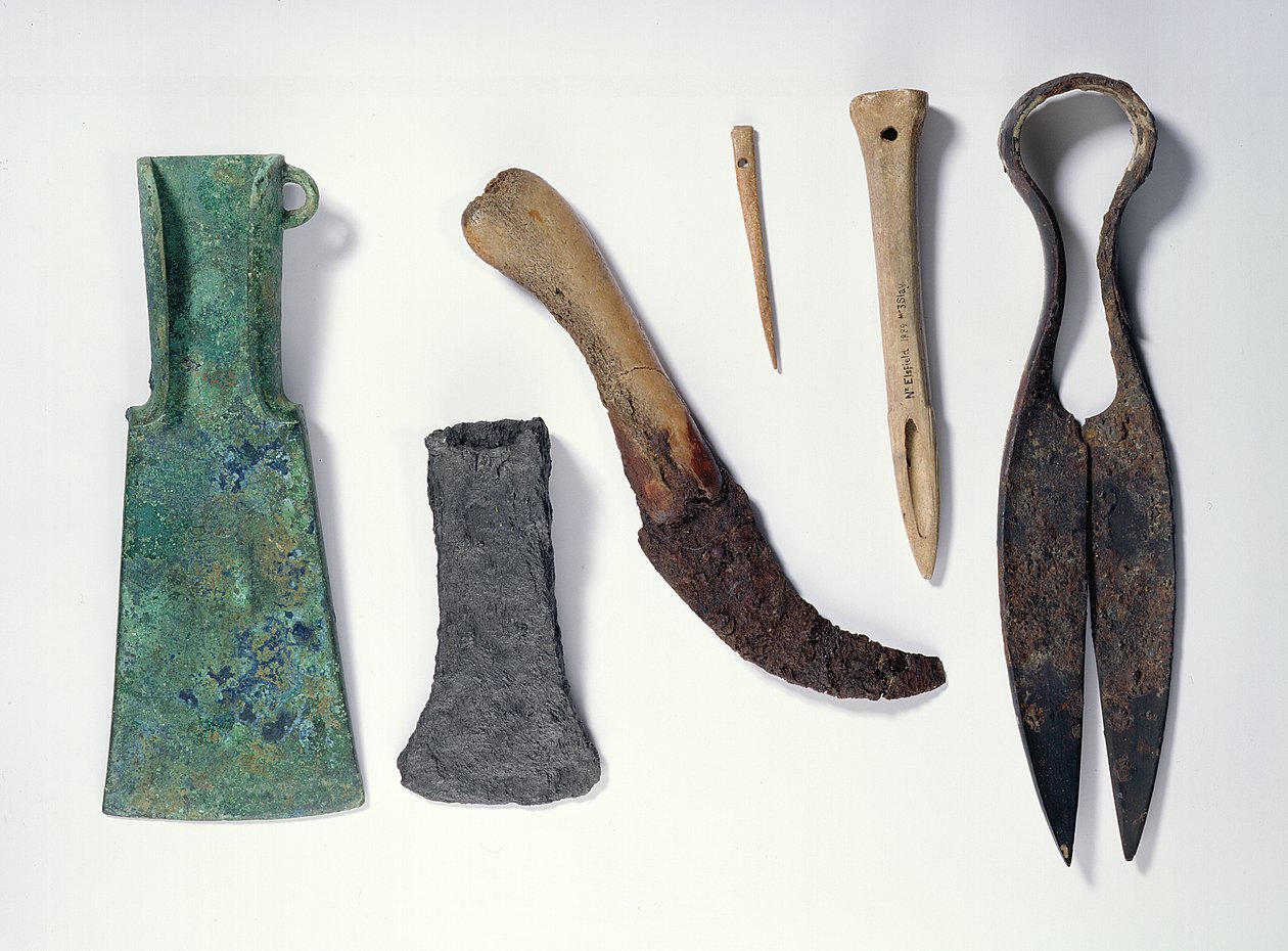 Selección de herramientas: de izquierda a derecha: hacha de bronce de la Edad del Hierro temprana con alas dobladas; hacha de hierro posterior; cuchillo con mango de hueso; aguja de hueso; punzón de hueso; tijeras de hierro de Iron Age