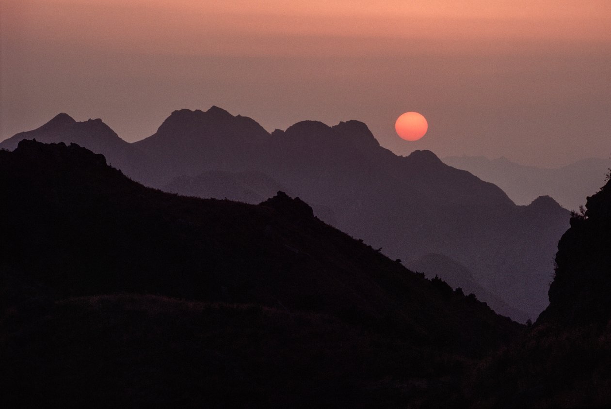 Un brillante sol carmesí anaranjado se pone sobre la cordillera de Yan Shan. Paso de Shanhaiguan, H... de James L Stanfield