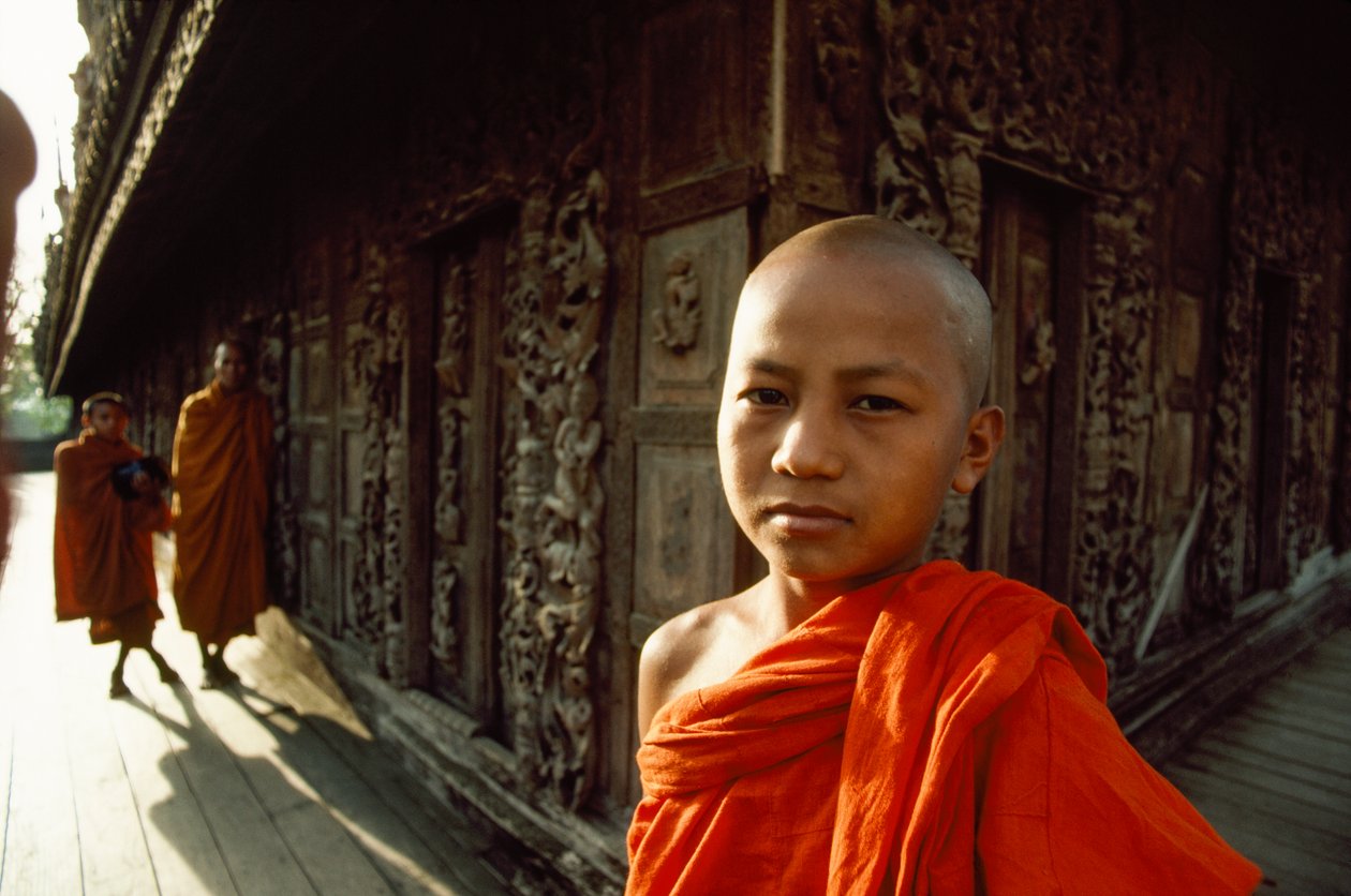 Un joven monje novicio ante unos paneles de teca tallada. Monasterio de Shwenandaw, Mandalay, Birmania. de James L Stanfield
