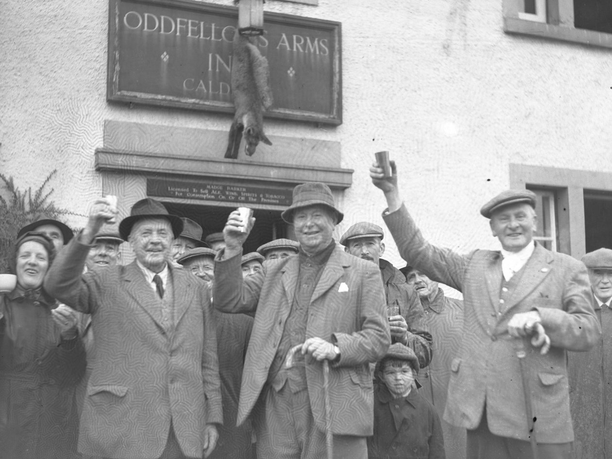 Un grupo de hombres, mujeres y niños levantan copas en señal de celebración frente a la posada Oddfellows. de Joseph Hardman