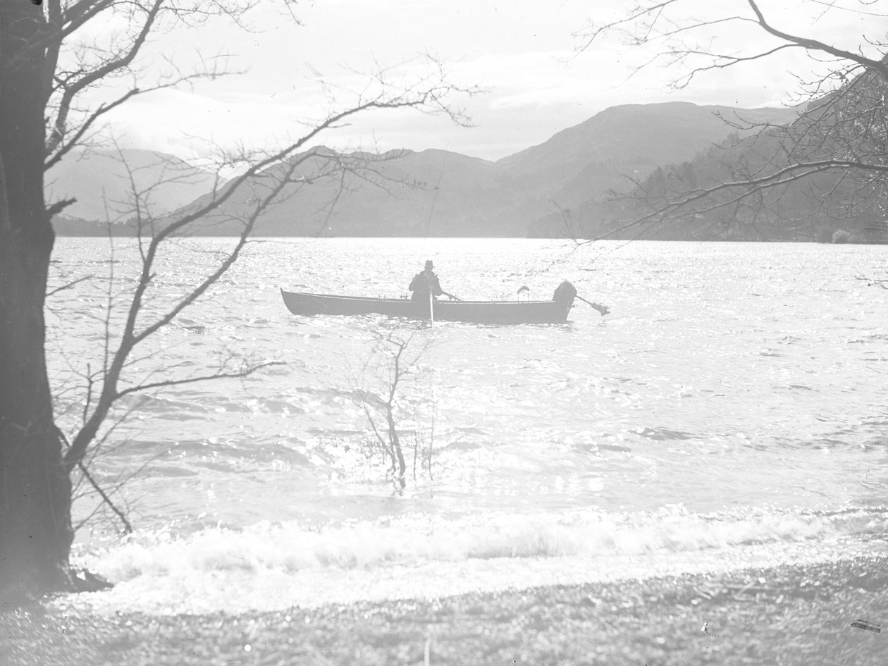 Un hombre sentado en una barca en un lago pescando, con fells al fondo de Joseph Hardman