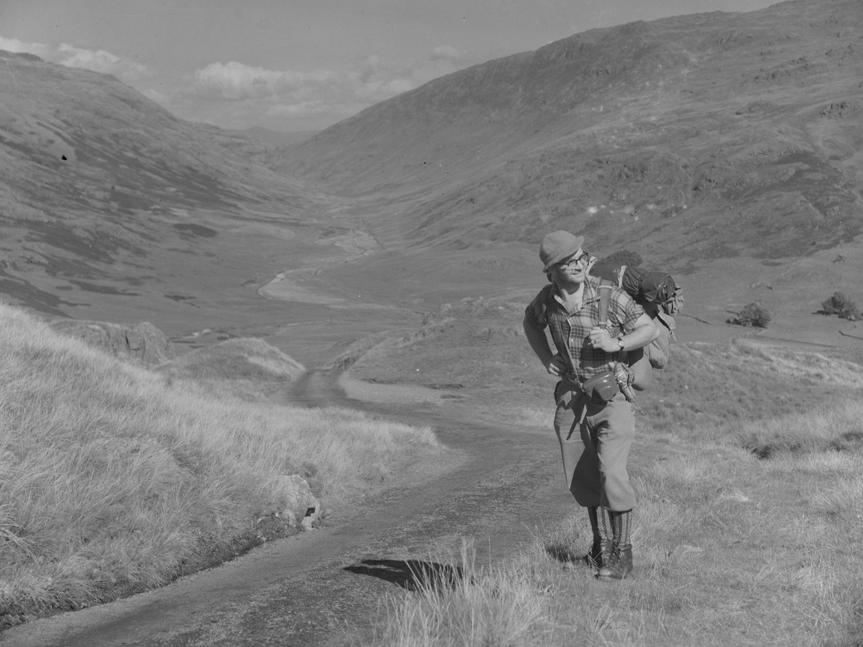 Un hombre camina con una mochila a la espalda en un paisaje de valle abierto de Joseph Hardman