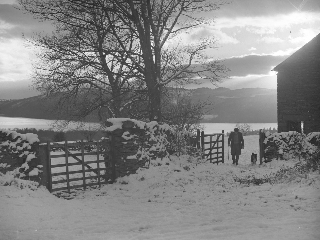 Hombre y perro caminando por la puerta hacia la cámara en la nieve con Thirlmere detrás de Joseph Hardman