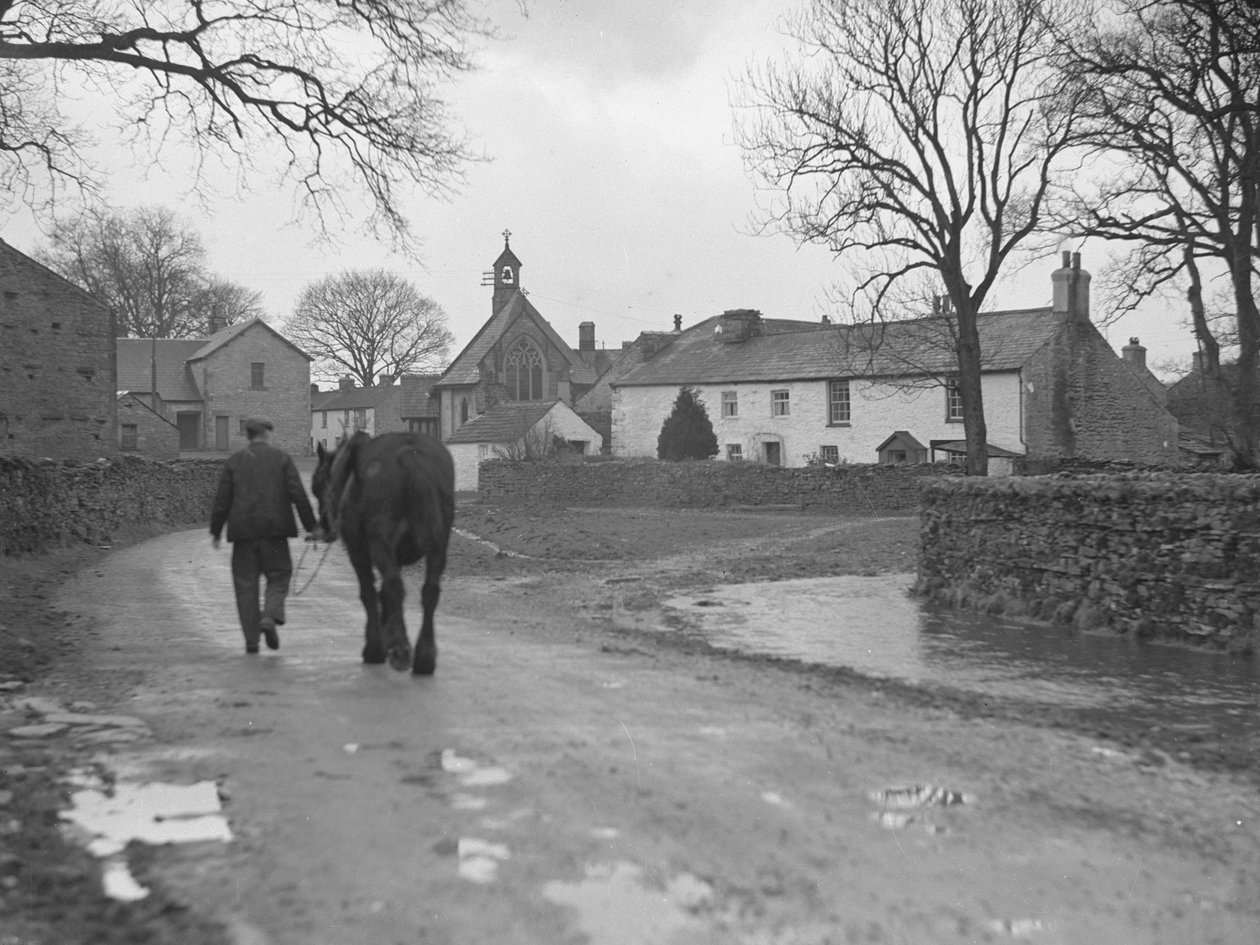 Hombre conduciendo caballo por la carretera lejos de la cámara hacia los edificios del pueblo y la iglesia; arquitectura; religiosa; eclesiástica; de Joseph Hardman