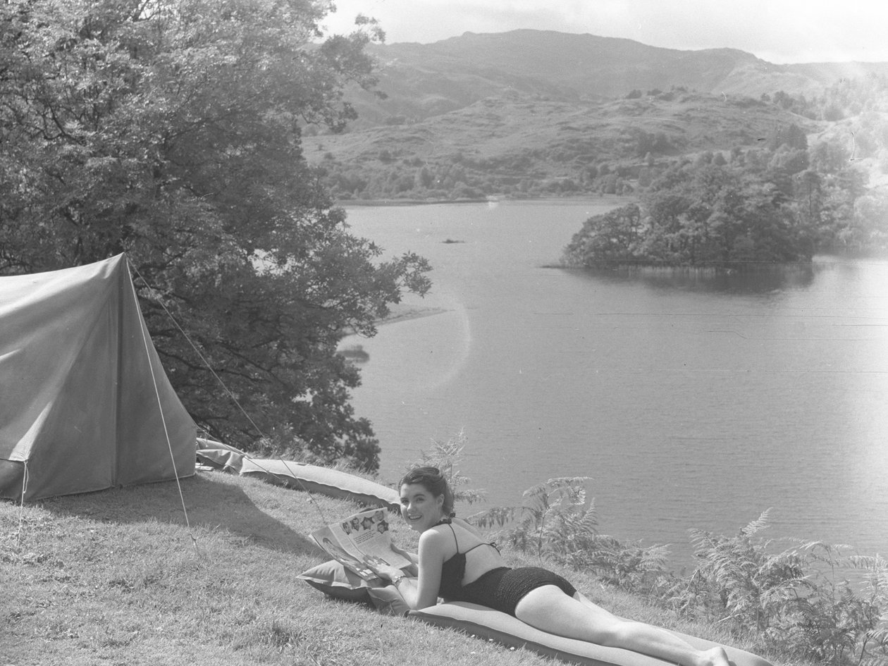 Vista de una joven en traje de baño tumbada en una colchoneta, con un lago al fondo. de Joseph Hardman