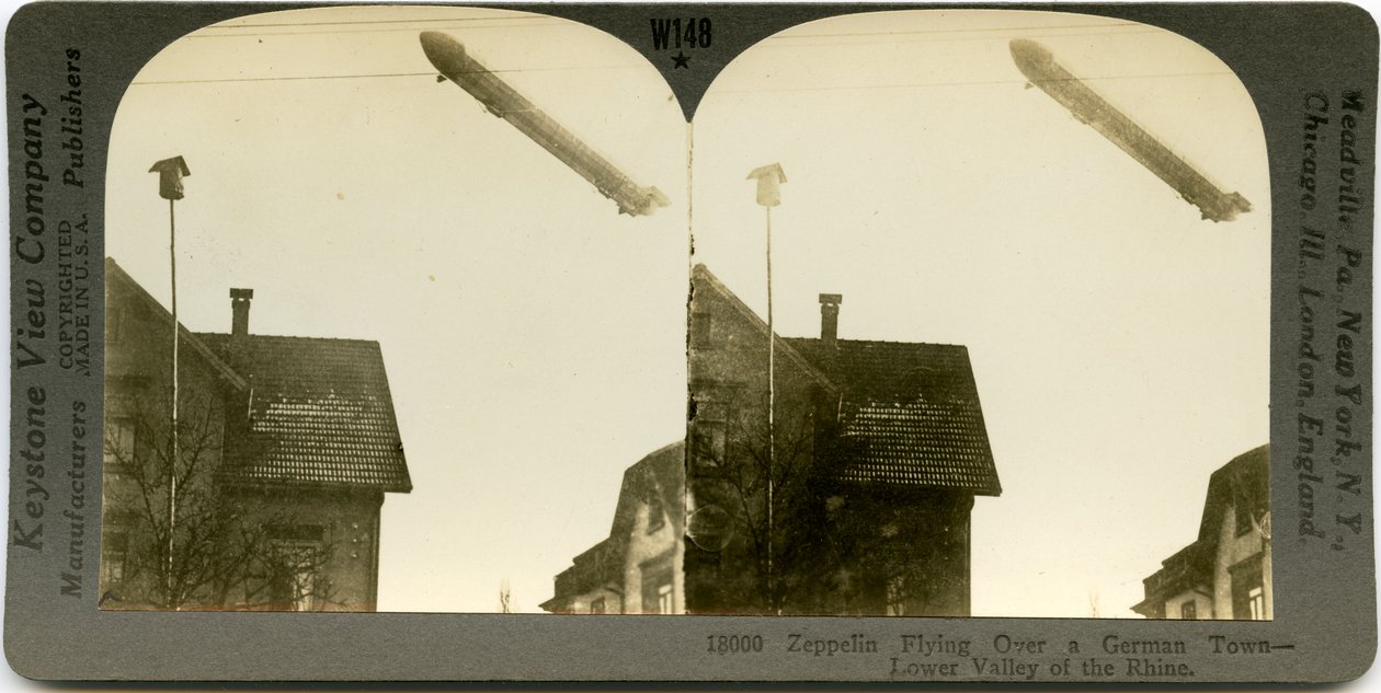 Tarjeta estereoscópica horizontal, sepia, mostrando un Zeppelin volando sobre los techos de una ciudad. Número de estereografía de Keystone 18000. El título dice de Keystone View Company