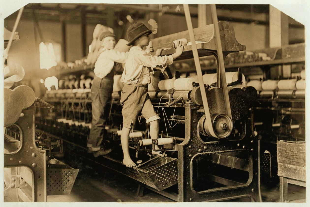 Niños pequeños trepando en el marco giratorio para arreglar hilos rotos y reemplazar bobinas vacías en Bibb Mill, Macon, Georgia, 1909 de Lewis Wickes Hine
