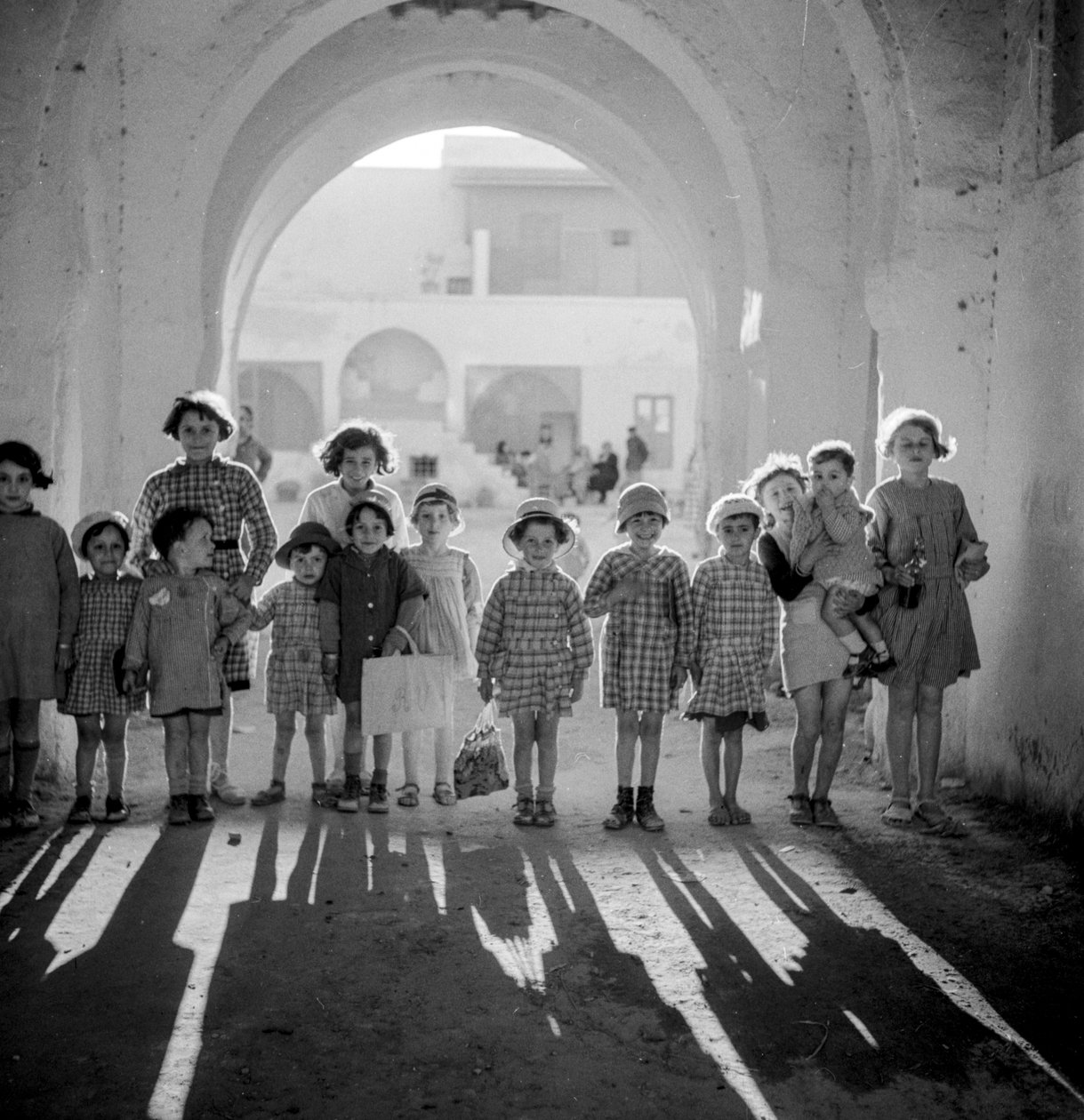 Niños europeos en uniforme escolar bajo arco con sombras. de Maynard Owen Williams