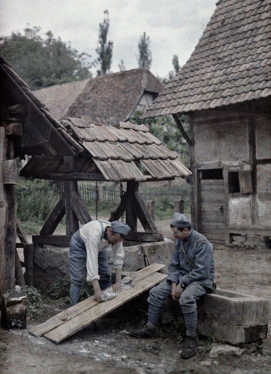 Dos soldados franceses cuidando su ropa usando tablas colocadas en el abrevadero de una fuente cerca de una granja en la ciudad de Gildwiller, Departamento Haut-Rhin, Alsacia, Francia, 21 de junio de 1917 (autocromo) de Paul Castelnau