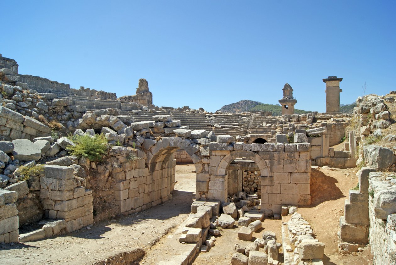Vista a través de la entrada abovedada del teatro de Xanthos hacia el foso de la Orquesta, mostrando la columna y la tumba de la Arpía, Xanthos, Turquía de Roman
