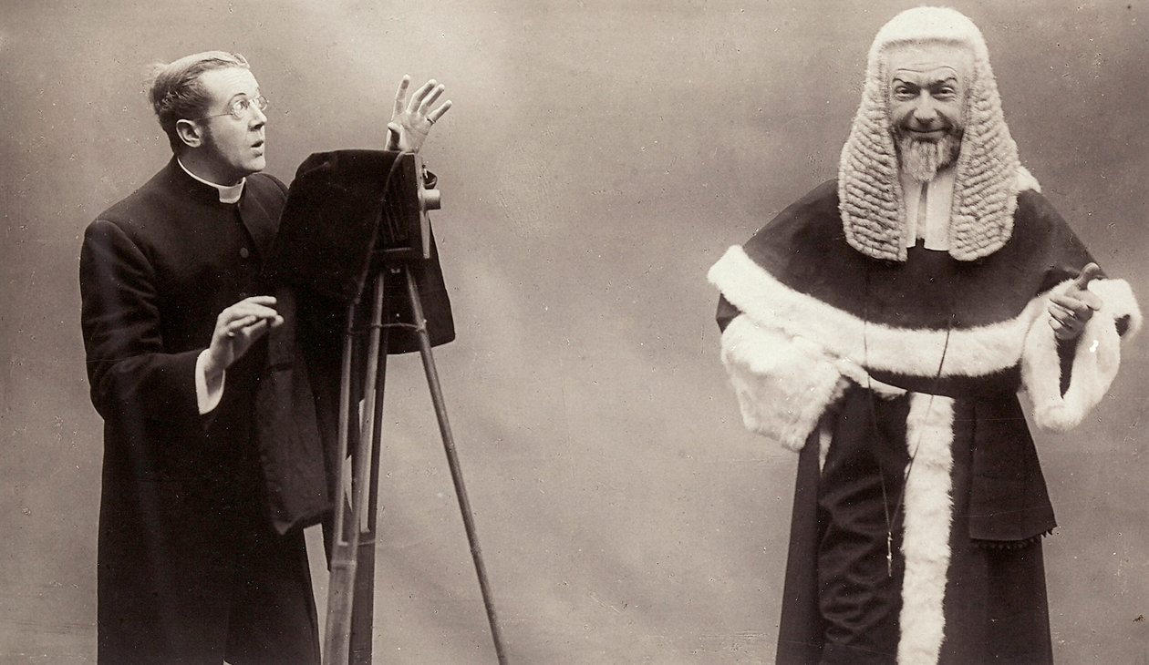 Un hombre con sotana apunta la lente de su cámara a un hombre vestido como un papa de Rotary Photographic Co Ltd