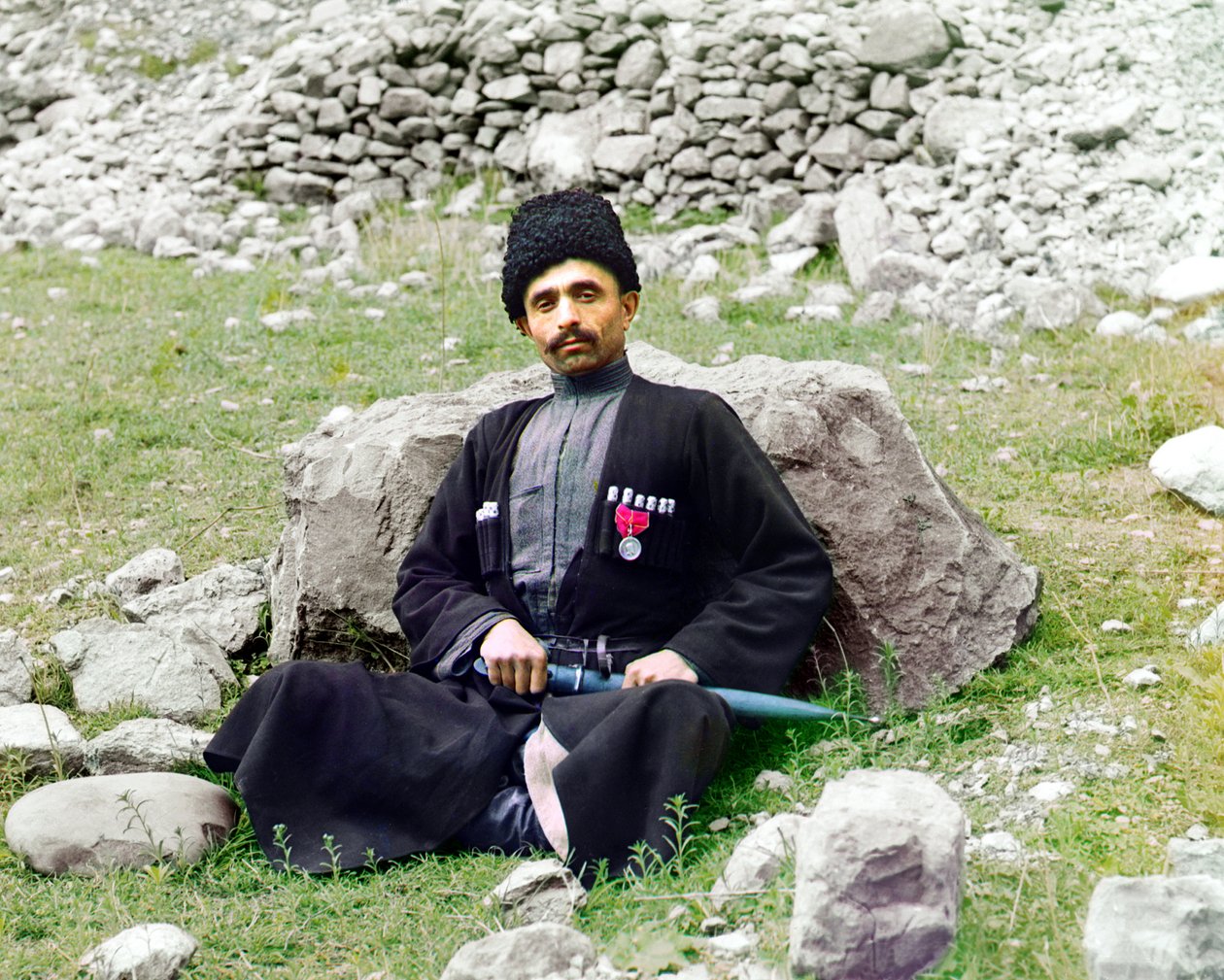 Tipos de Daguestán - Hombre musulmán suní con vestimenta y tocado tradicional, con una daga envainada a su lado, sentado en el suelo, Imperio Ruso, entre 1905 y 1915 de Sergey Prokudin Gorsky