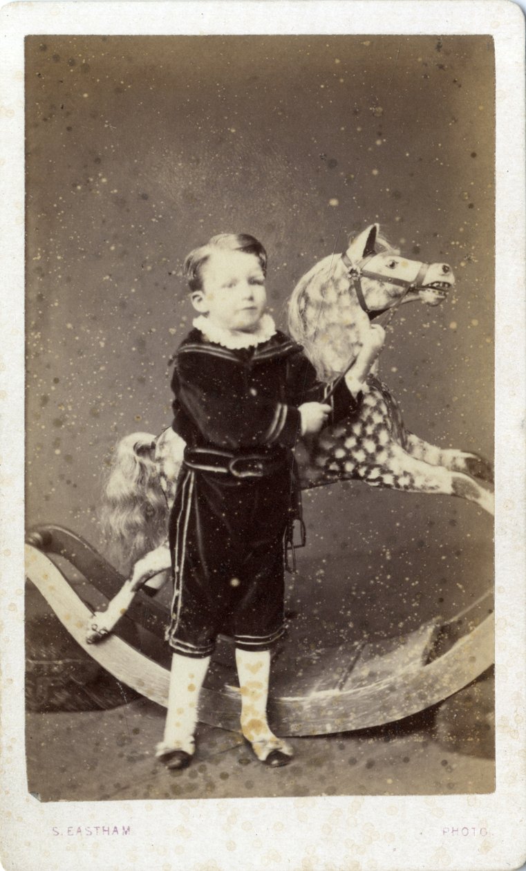 Niño pequeño de pie junto a un caballo de juguete de Silas Eastham