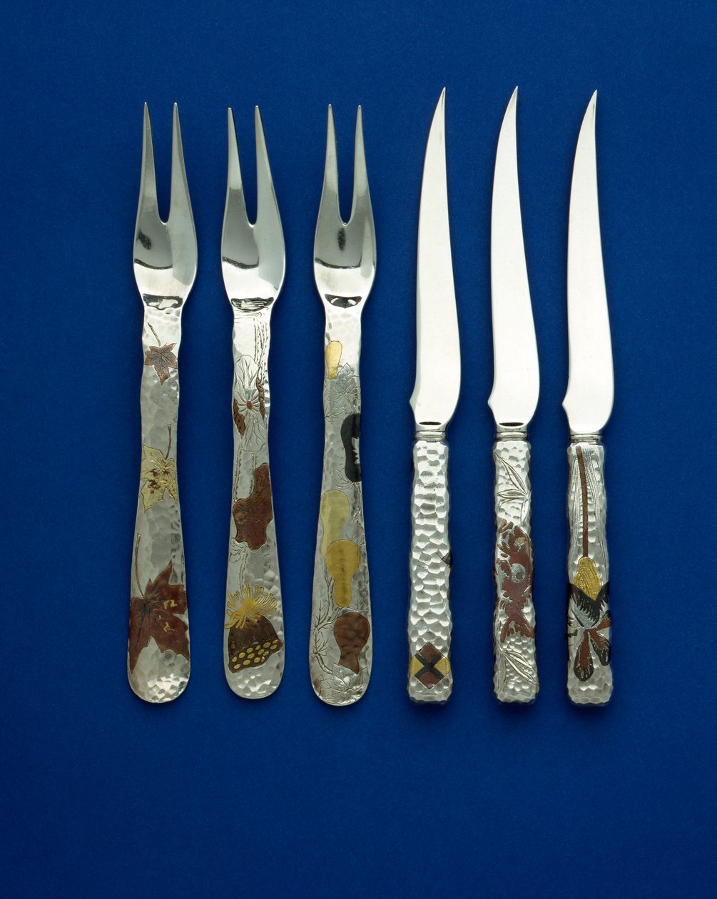 Parte de un fino y raro conjunto de 36 cuchillos y tenedores de postre, los mangos martillados con incrustaciones de cobre patinado y oro de varios colores, con detalles grabados de varios diseños florales, animales y geométricos, c.1880 de Tiffany and Company