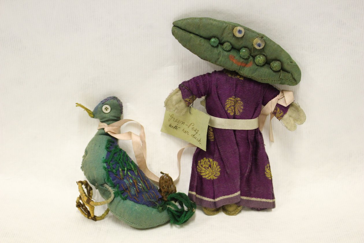 Muñeca de trapo Miss Green Peas, la cabeza tiene forma de vaina de guisante y lleva a su patito mascota por una cinta de raso rosa. de Una Maw