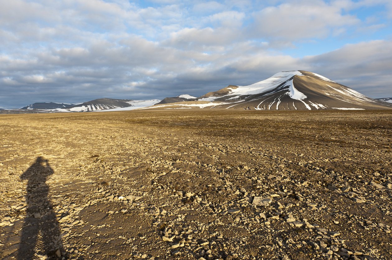 Sombra de un humano, suelo estructural poligonal en el Plataberget, pico nevado Nordenskjoeldfjellet en el fondo, cerca de Longyearbyen, Spitsbergen, Svalbard, Noruega, Europa de Unbekannt
