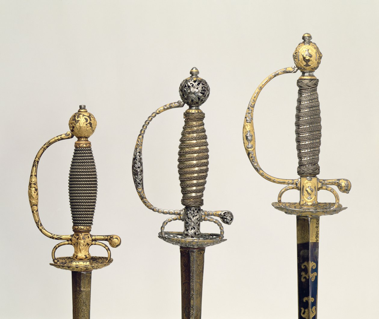 Empuñaduras de tres espadas francesas: una de acero, azulada y sobrepuesta con diseños en oro cincelado, c.1730; una de acero perforado y cincelado y el fondo de oro mate, c.1760; una de acero cincelado de Unbekannt Unbekannt