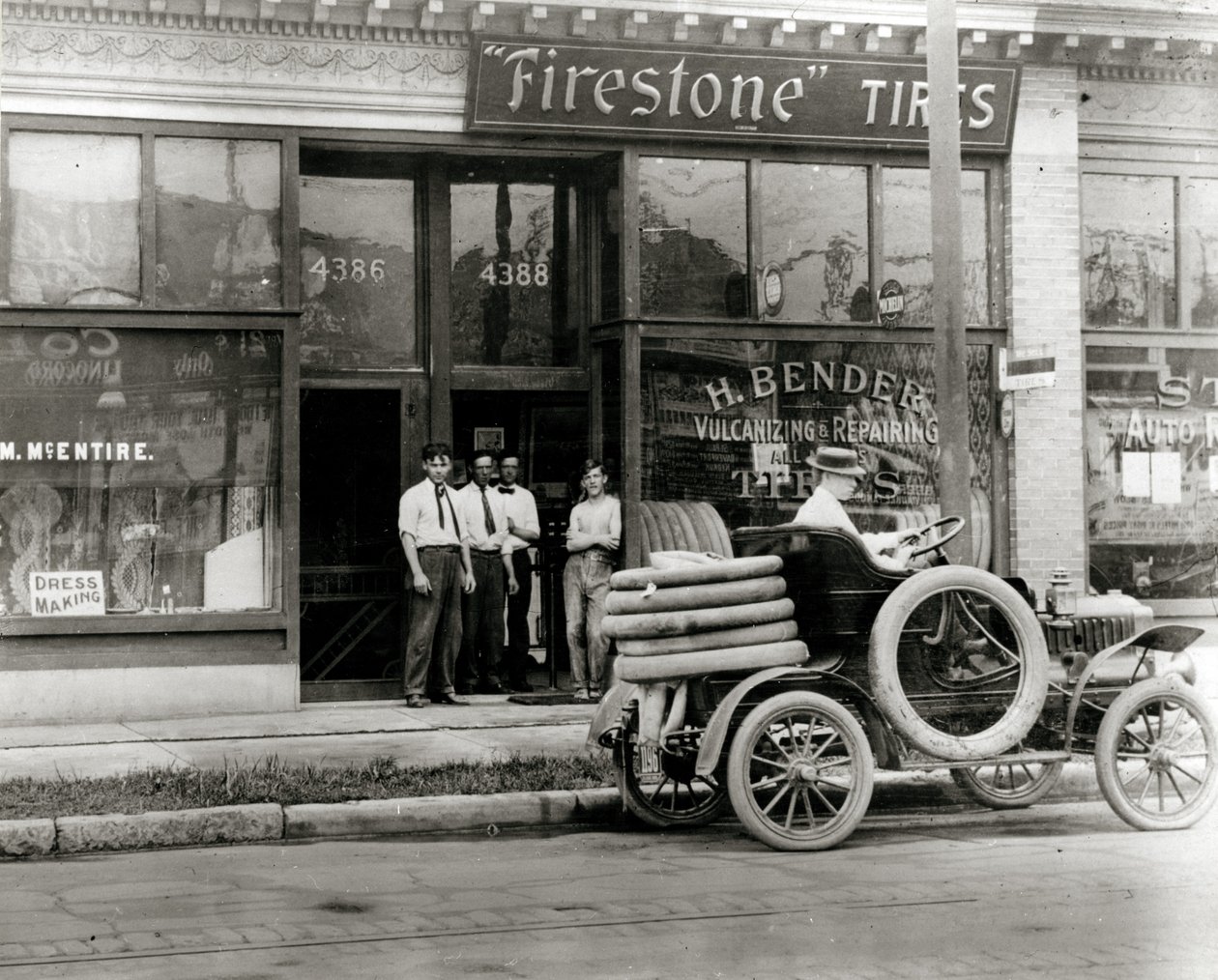 Hombres y camión de reparación de neumáticos reunidos fuera del concesionario de neumáticos H. Bender Firestone en 4388 Olive Street de Unknown
